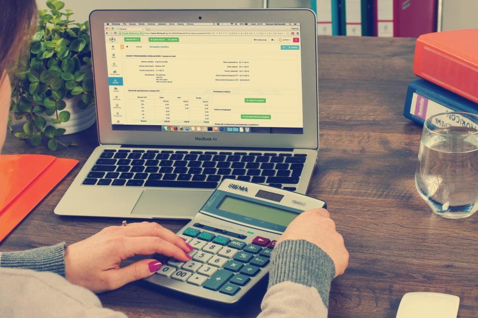 Accountant using a calculator next to a laptop showing a spreadsheet